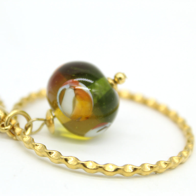 zoom sur perle du Collier long Salvia avec pendentif cercle en acier doré et perle en verre de Murano bicolore topaz et olive.